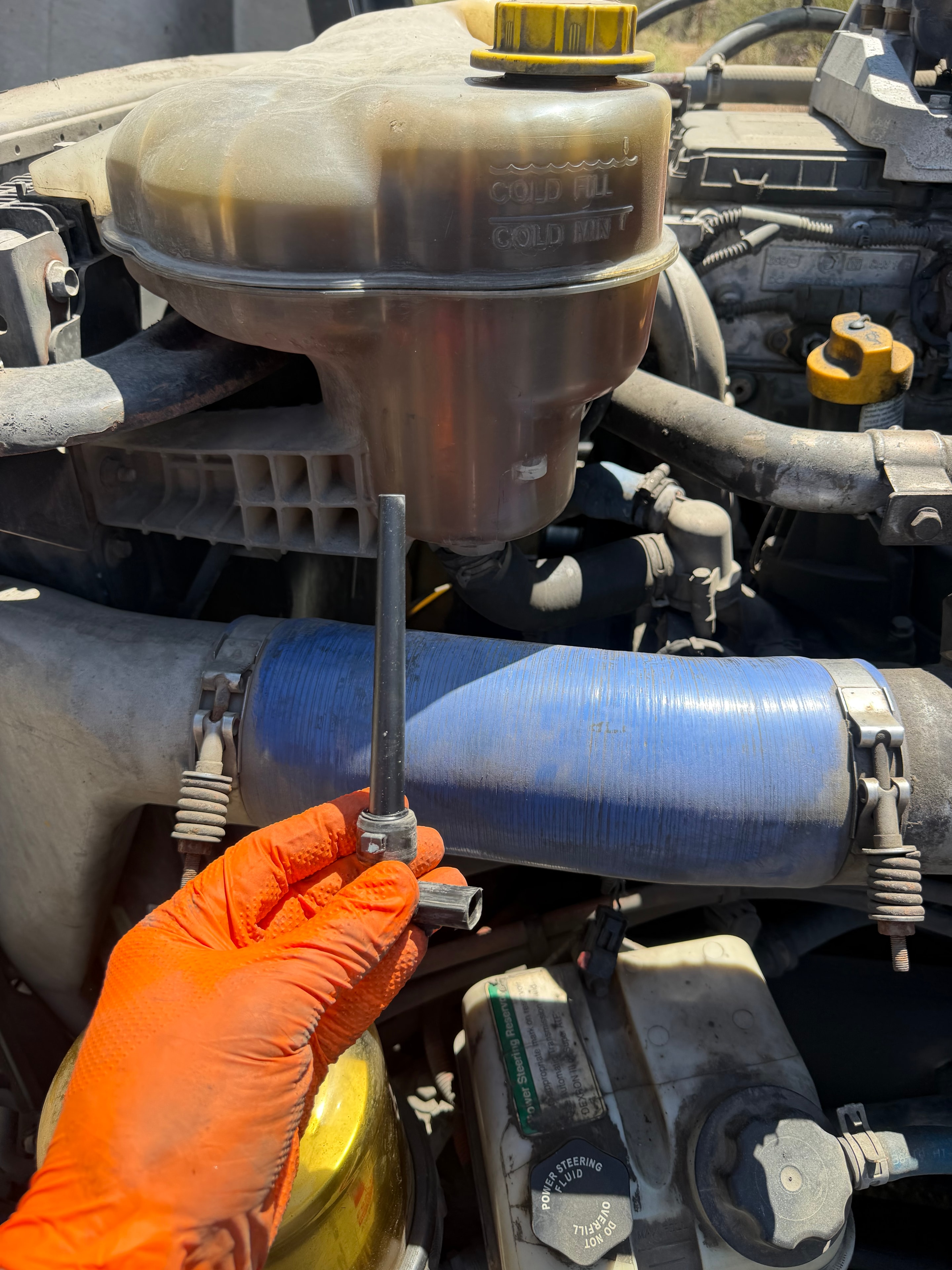 RoadWrench mobile semi truck mechanic replacing faulty coolant level sensor on Freightliner Cascadia engine — hands-on coolant reservoir sensor swap during roadside repair in Mesa AZ to fix engine protection shutdown fault